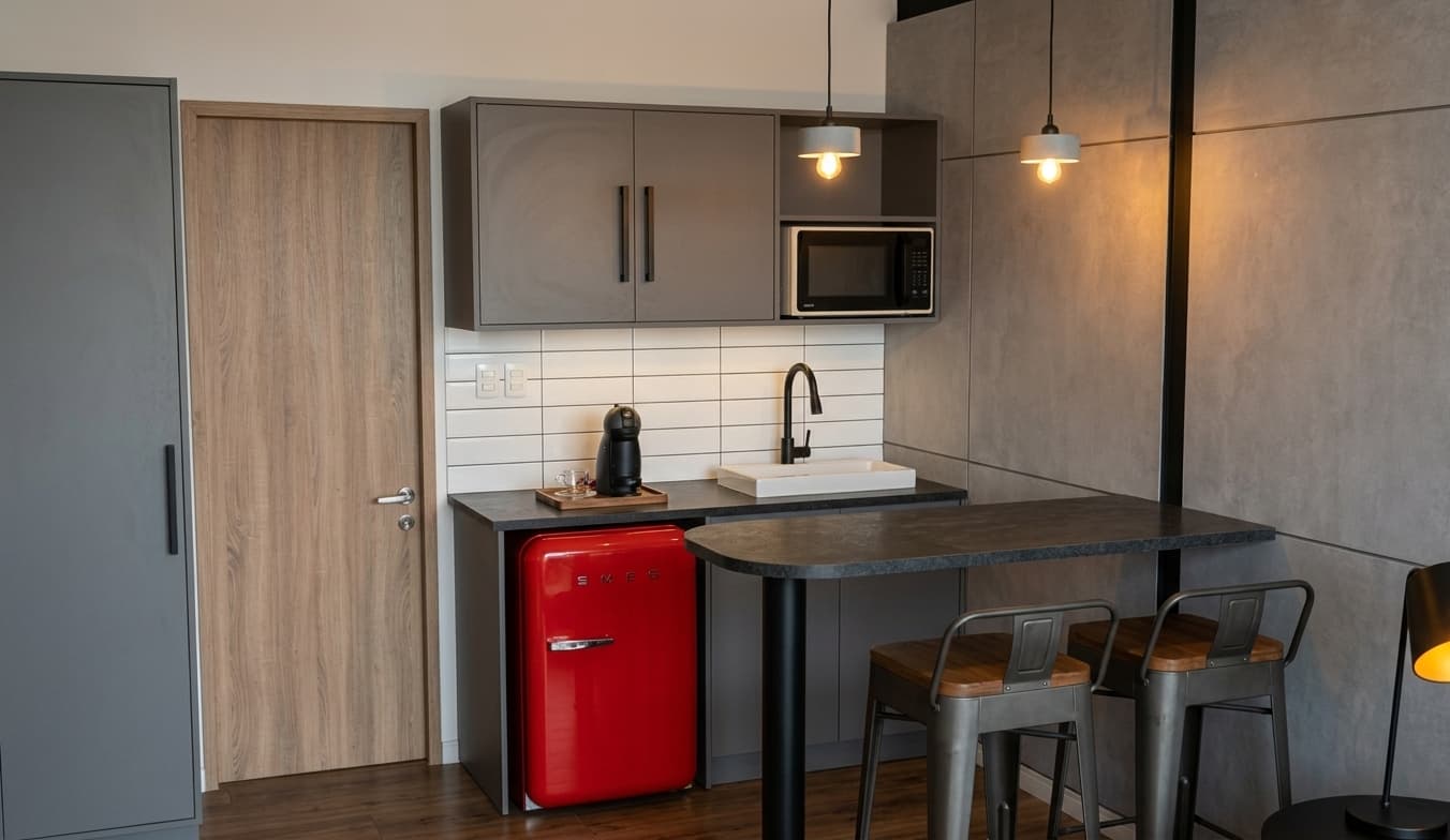 Kitchenette de CRUDO 02 con bacha, microondas, heladera compacta roja y barra con banquetas