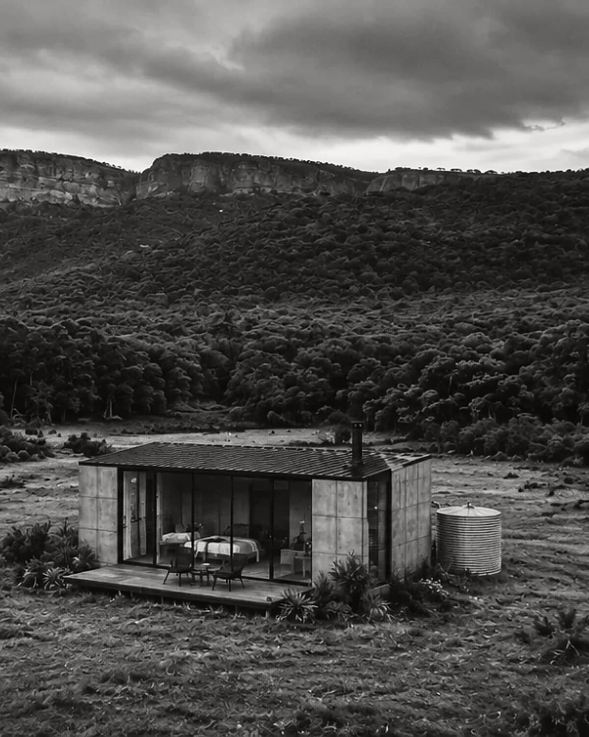 Casa CRUDO terminada en el campo, con frente vidriado, deck de madera y tanque de agua