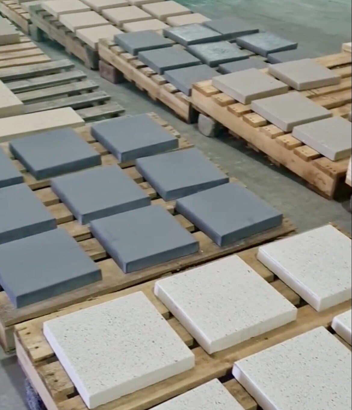 Placas de concreto en distintos colores y texturas, secándose sobre pallets